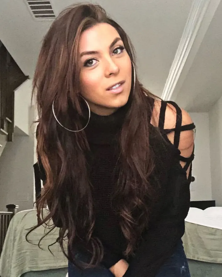 Femme aux cheveux bruns en haut noir à découpes, regardant l'appareil photo dans une chambre