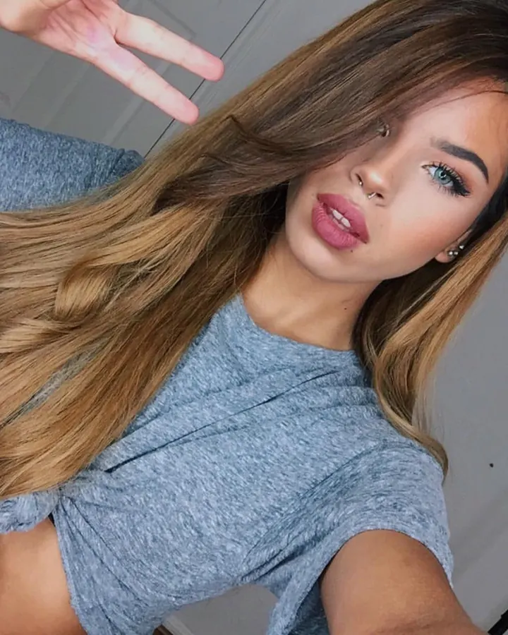 Jeune femme blonde, en tenue décontractée, prenant un selfie dans un cadre intérieur.