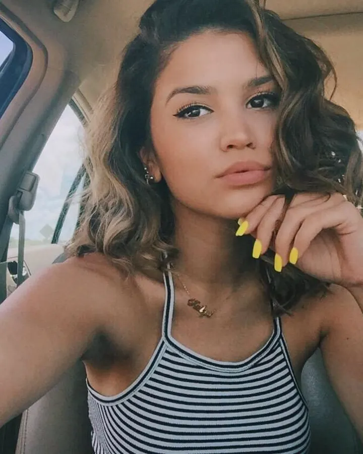 Femme aux cheveux châtains assise dans une voiture, portant un haut rayé noir et blanc, regardant la caméra.