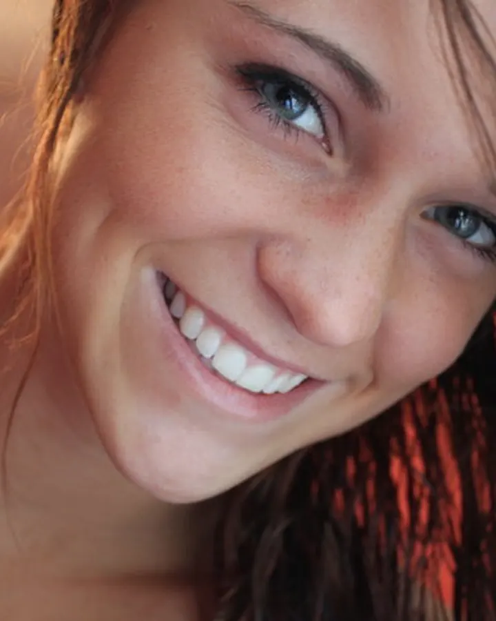 Femme aux cheveux blonds souriant, en gros plan, avec une lumière chaude derrière elle