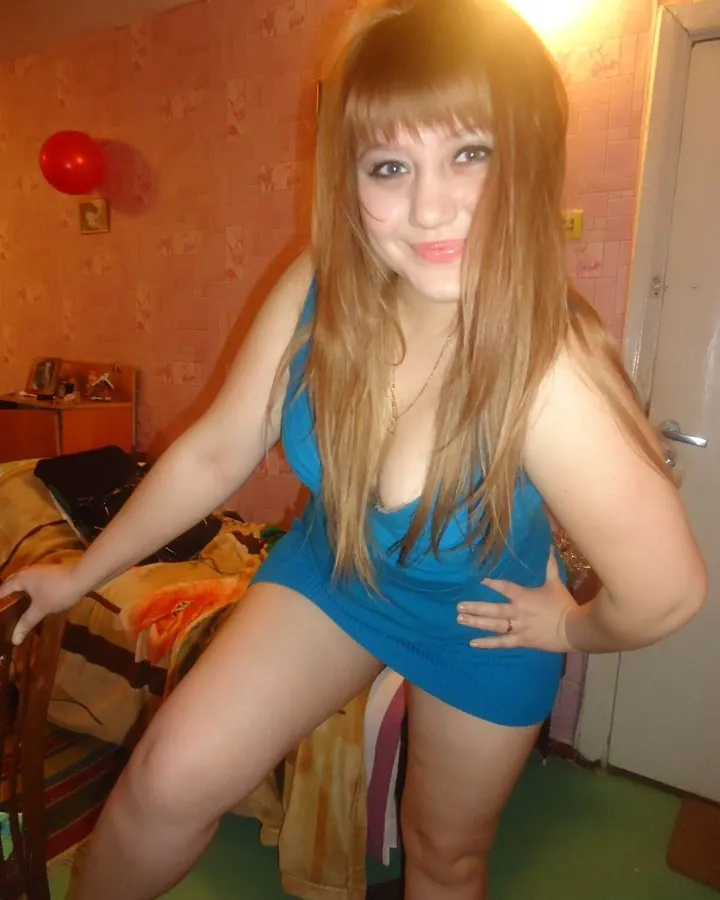 Femme aux cheveux bruns-noirs, en tenue rose, se tenant de profil près d'un mur.