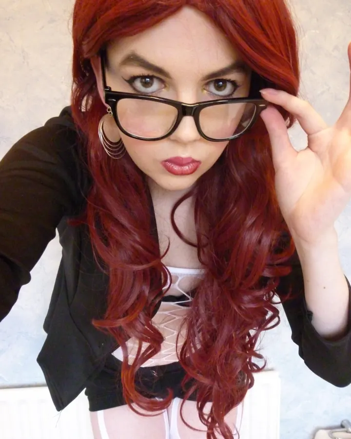 Femme aux cheveux roux, en tenue rose, se tenant de profil près d'un mur.