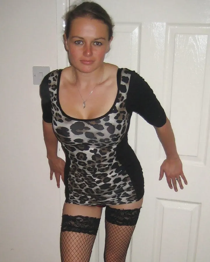 Femme en robe léopard avec manches noires, portant des collants à mailles et des bas noirs, debout devant une porte blanche.