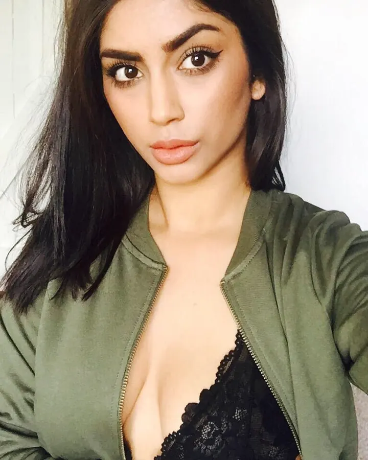 Femme aux cheveux foncés en veste verte, regardant l'appareil photo, buste découvert.