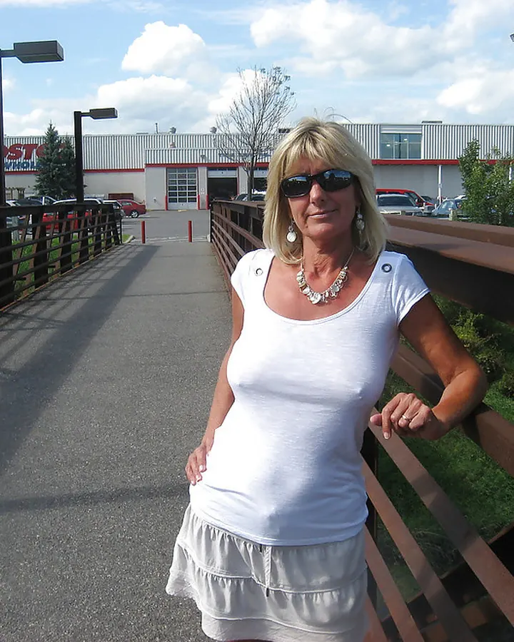 Femme blonde aux cheveux courts, vêtue d’un haut blanc et d’une jupe blanche, posant devant un magasin Costco.