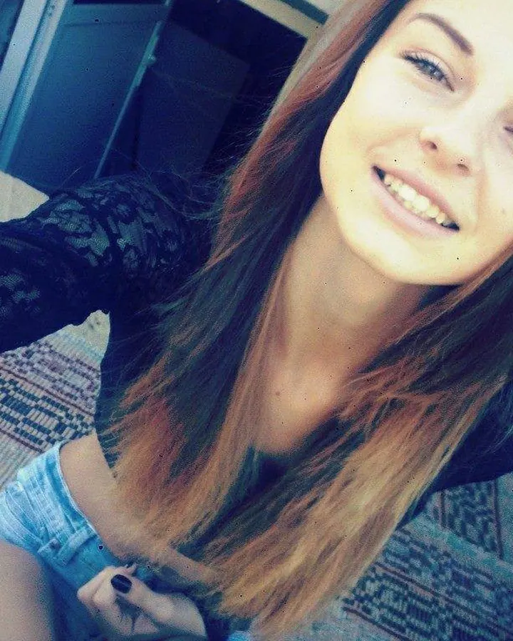 Jeune femme aux cheveux bruns, souriante, en tenue décontractée, prenant un selfie dans un intérieur.