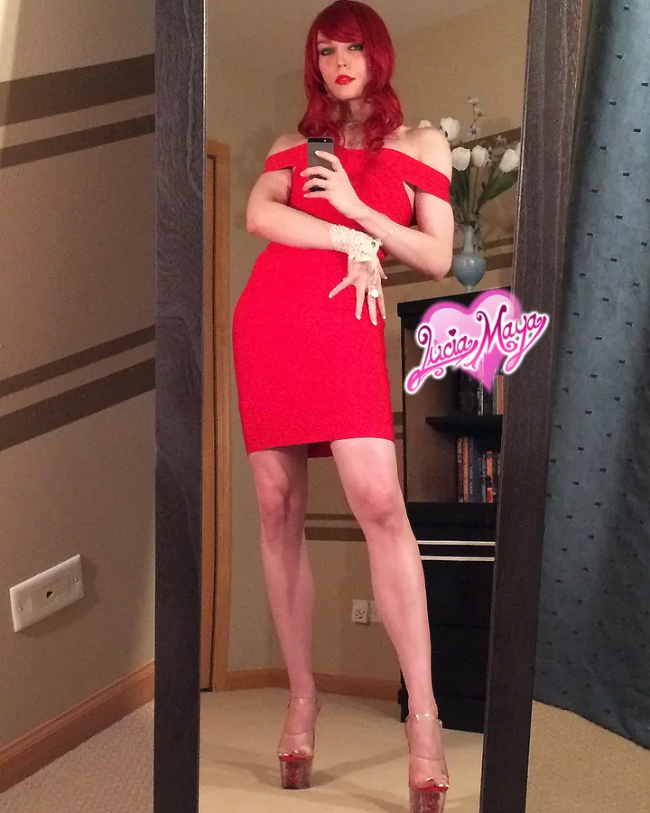 Femme aux cheveux roux portant une robe rouge, se prenant en photo dans un miroir, pieds nus sur des talons hauts.