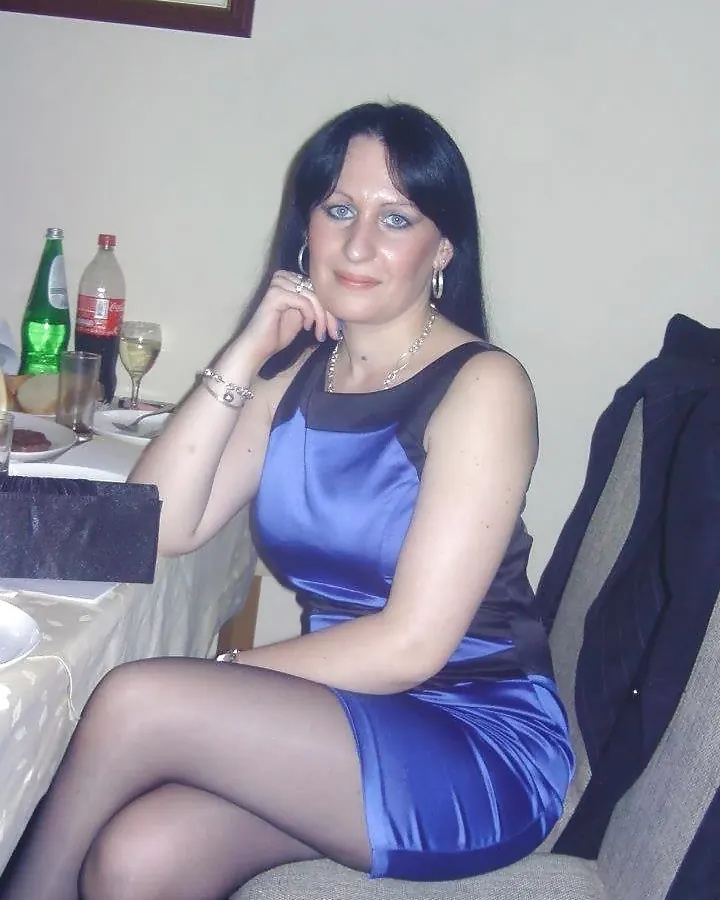 Femme aux cheveux bruns en robe bleue satinée, posant à table