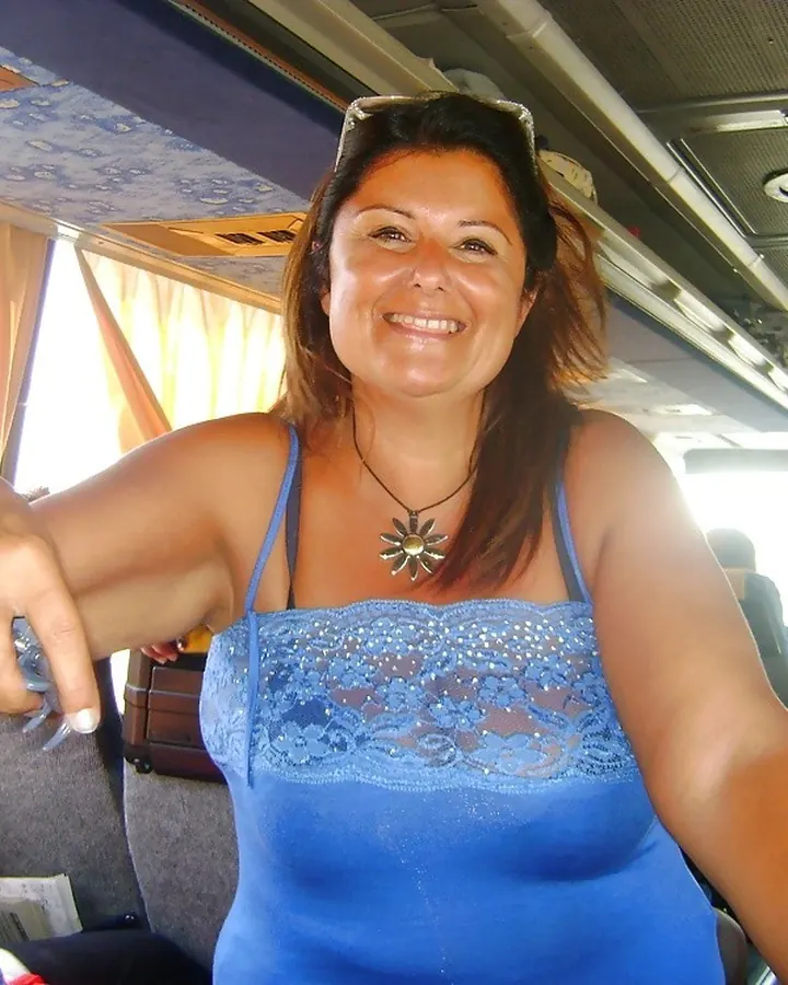 Femme souriante en débardeur bleu orné de dentelle, assise dans un bus.