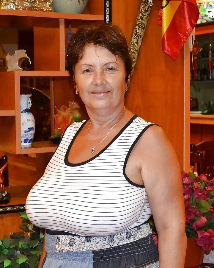 Femme aux cheveux longs bruns, vêtue d’un haut noir et d’un short en dentelle, posant de dos sur un lit coloré.