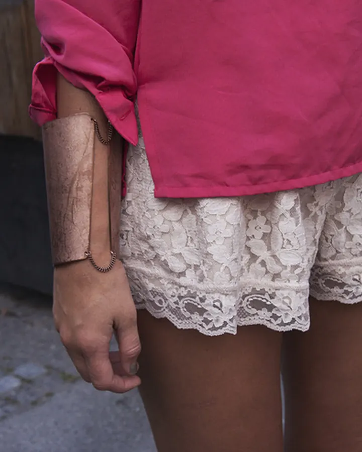 Femme portant un haut rose et une jupe en dentelle blanche, vue de la taille vers le bas sur un trottoir pavé.