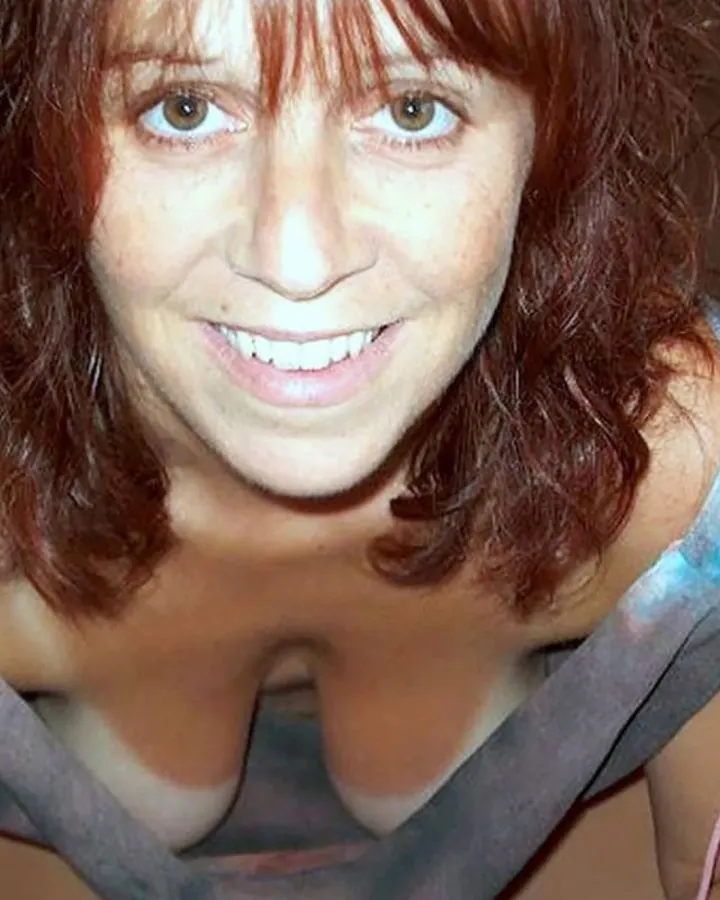 Femme aux cheveux roux en tenue légère, assise sur un sol carrelé, souriant vers l'objectif.