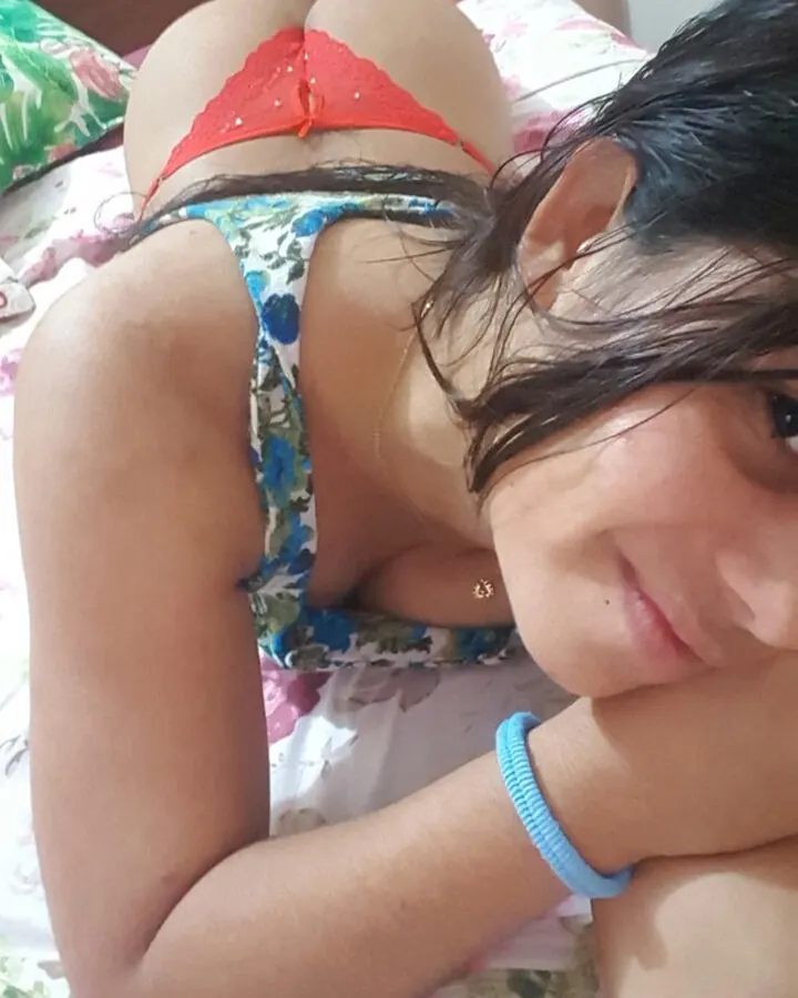 Jeune femme arabe en sous-vêtements floraux, allongée sur un lit, regardant vers la caméra, bracelet bleu au poignet