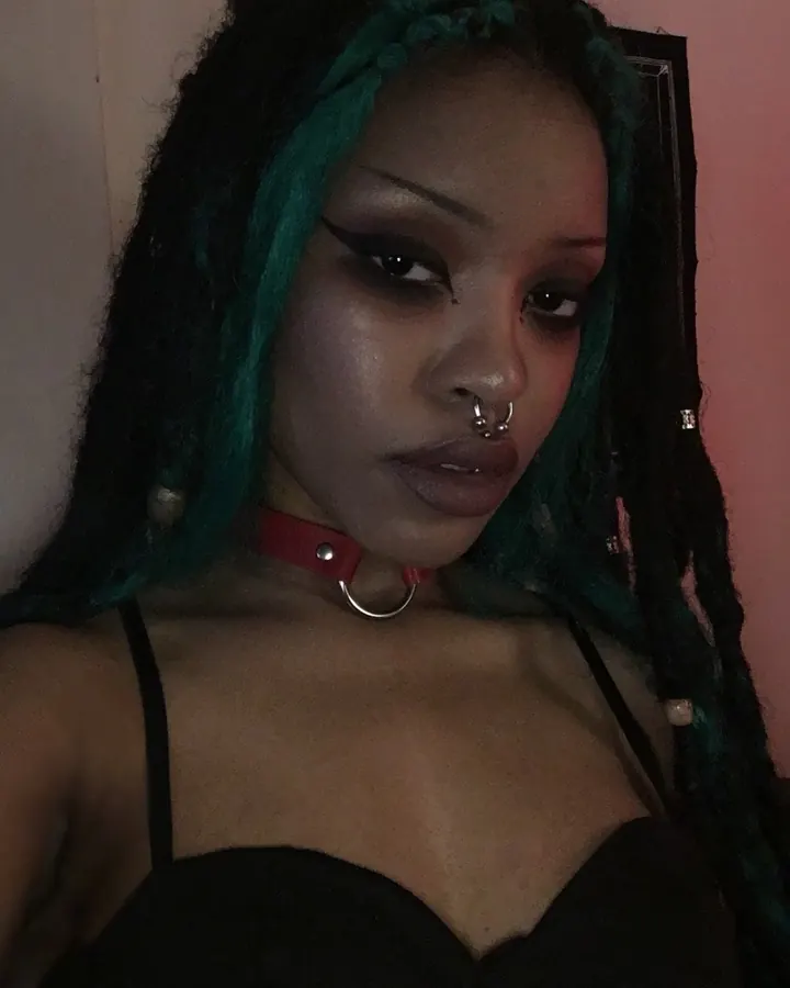 Femme africaine aux cheveux noirs avec des mèches vertes, portant un collier rouge, regardant directement l'appareil photo