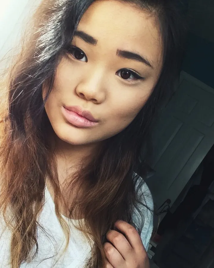 Femme aux cheveux châtains portant un haut blanc et un short bleu marine, prenant un selfie dans un miroir.