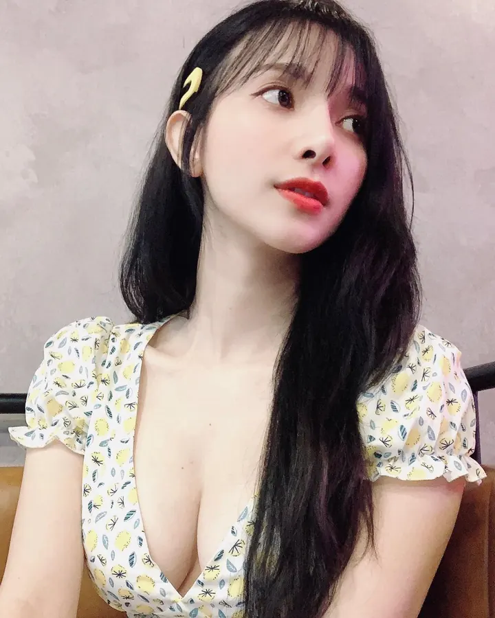 Femme aux longs cheveux noirs, portant une robe à motifs jaunes et verts, regardant de côté, avec un clip jaune dans les cheveux.